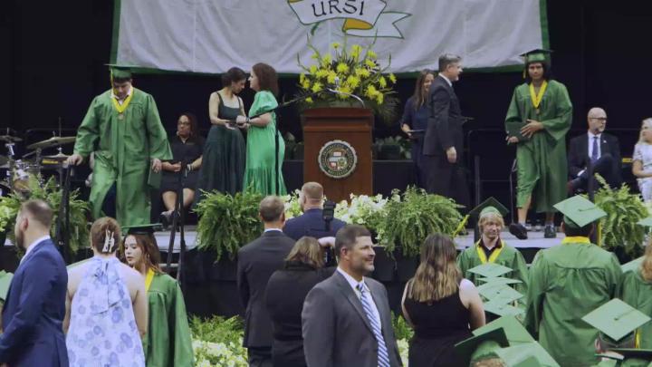 RBHS graduation stage, two graduates walk toward stairs.